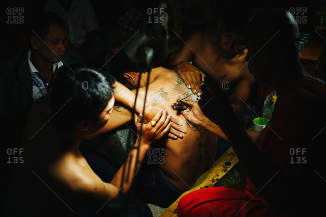 March 19, 2011: Group of people helping monk making "sak yant" traditional hand poked magic tattoo during Wai Khru festival in Wat Bang Phra, Thailand