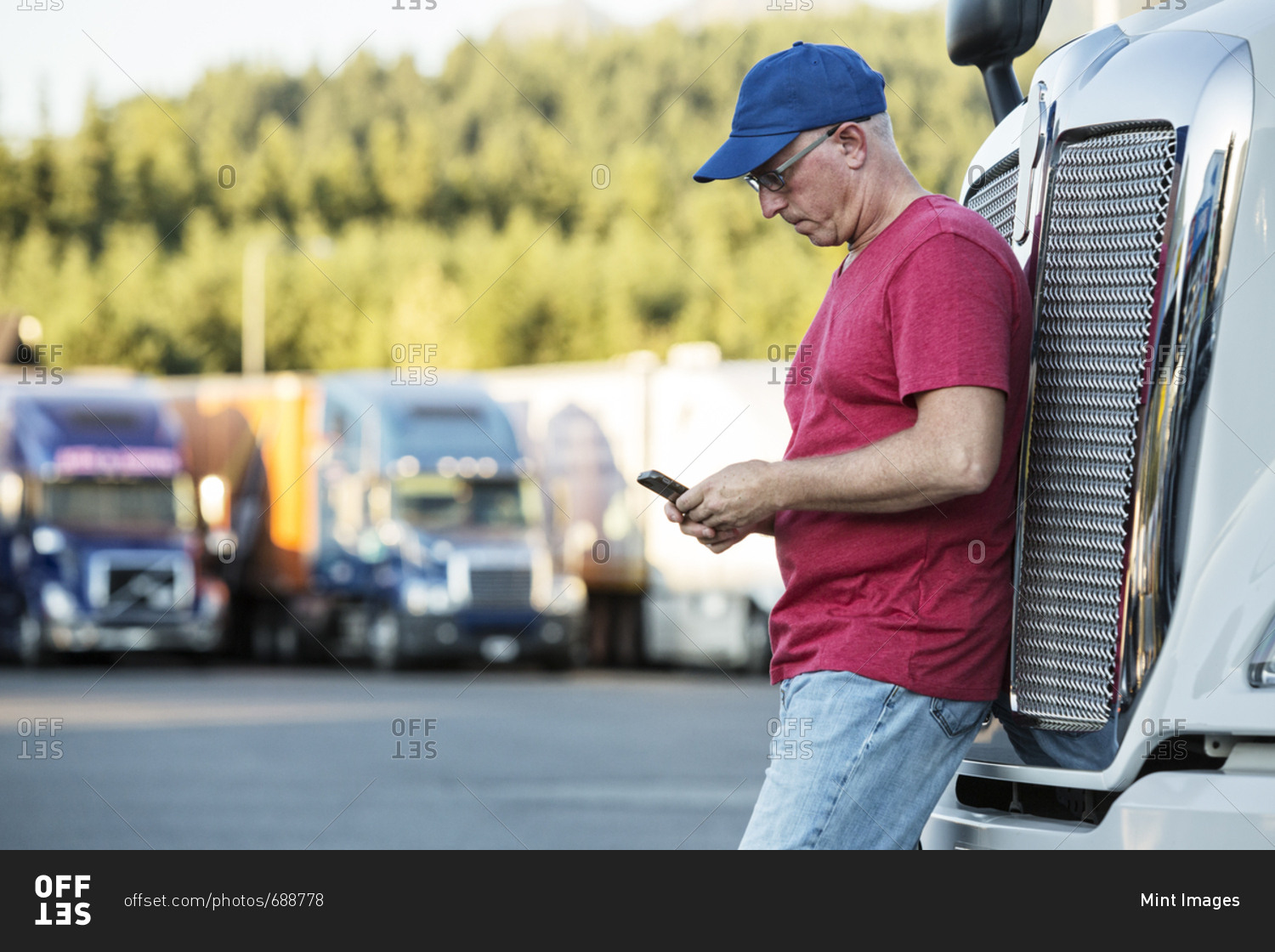Caucasian man truck driver texting while standing next to the grill of his commercial truck in a struck stop