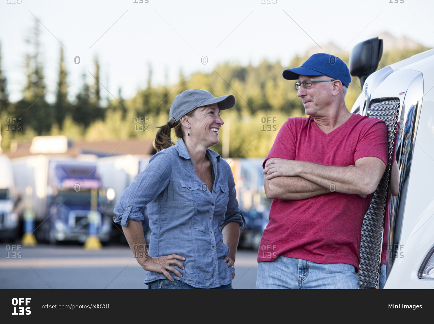 Caucasian man and woman driving team talking in front of a large truck at a truck stop