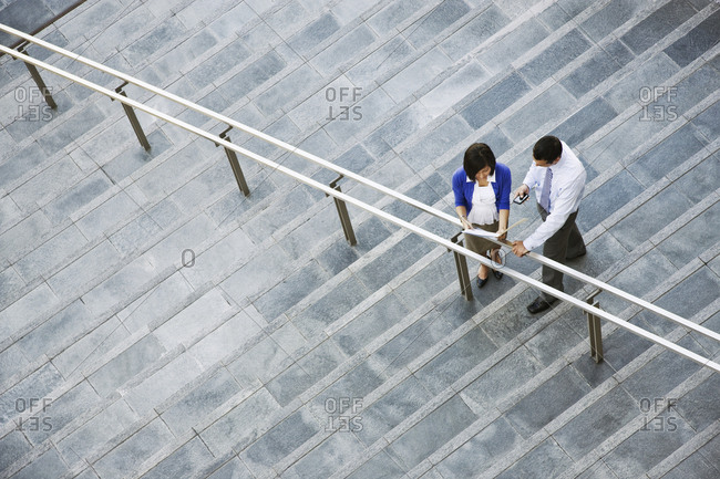 View from above looking down on a businesswoman and businessman standing on steps up to a large office building