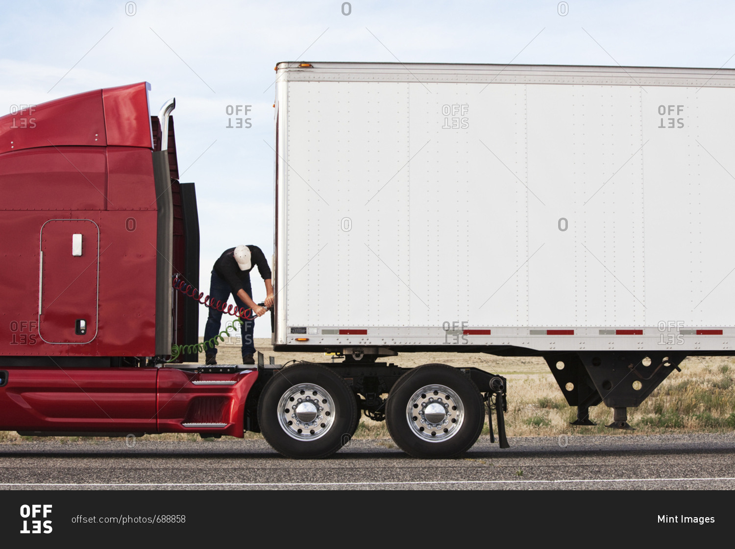 View of a driver connecting the power cables to trailer of a  commercial truck