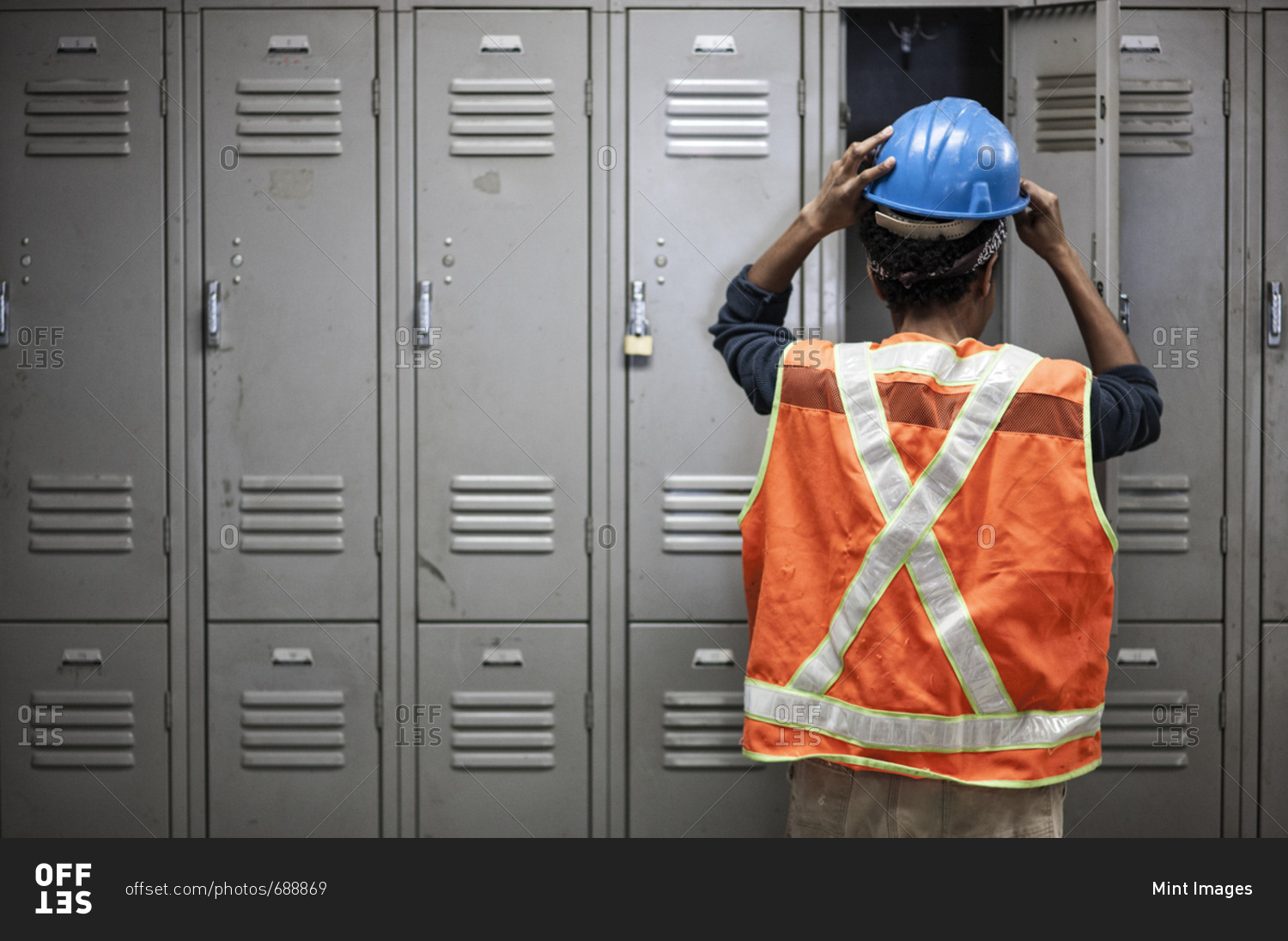 Factory worker wearing a safety vest getting ready for work next to locker in the break room