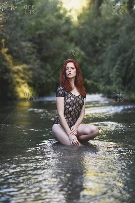 Portrait of redheaded young woman wearing transparent black bodysuit crouching in water