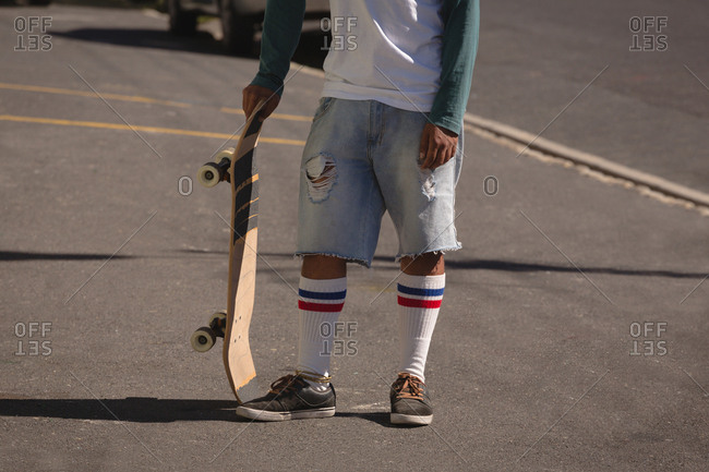Man standing with skateboard in street on a sunny day