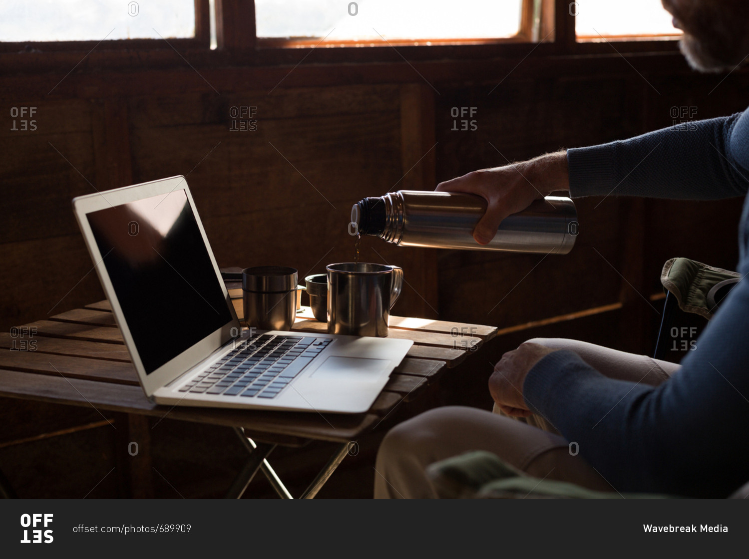 Mid section of man pouring coffee from vacuum flask at desk