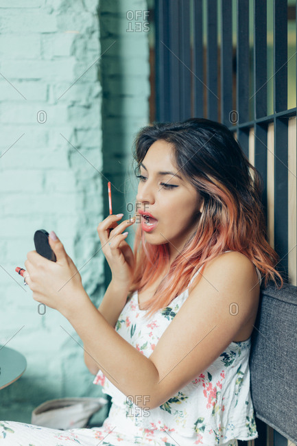 Young hispanic woman re-doing her lip stick outside a cafe