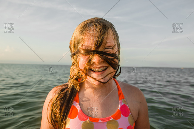 Portrait of young girl with braces and her over her face as she emerges from water