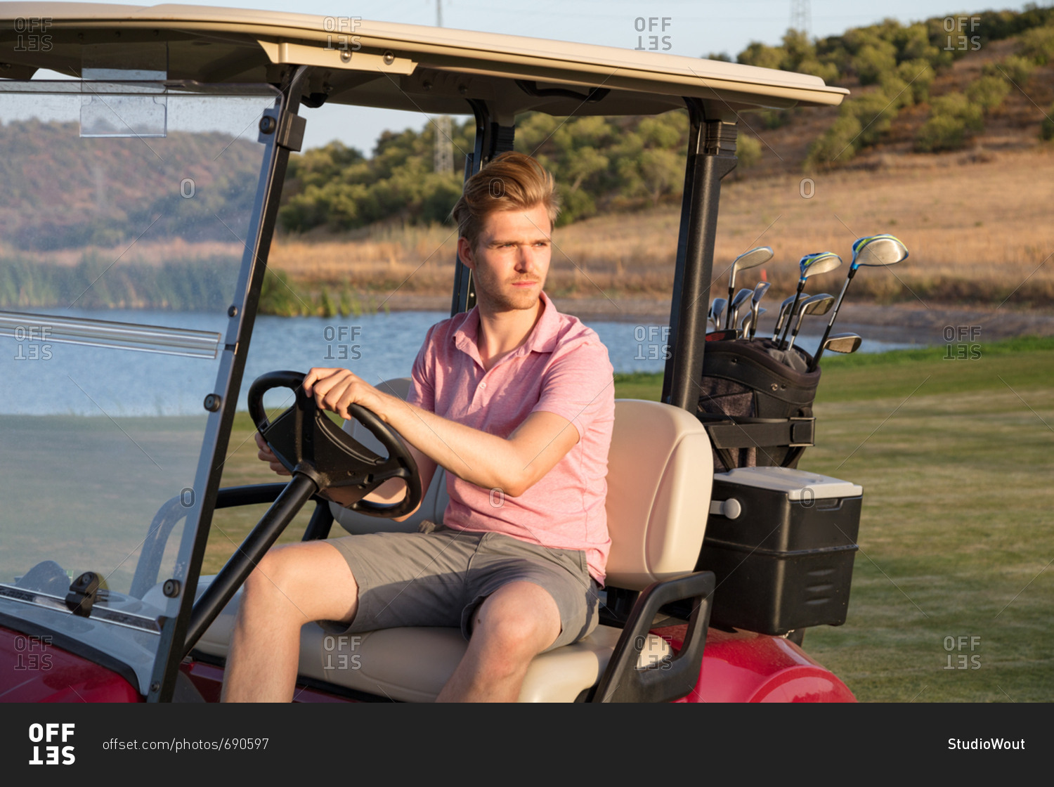 Young handsome golfer driving golf cart with bag of clubs