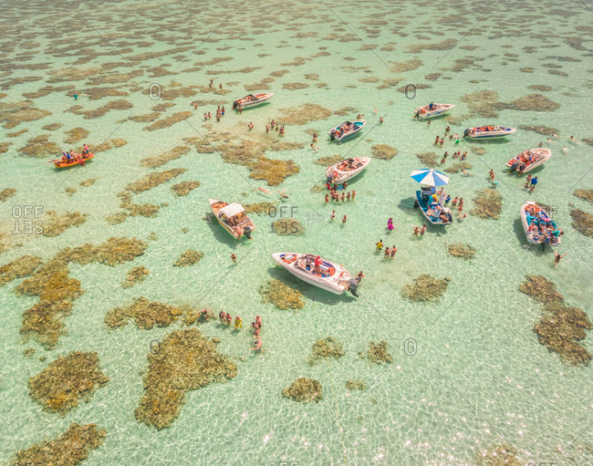 Aerial view of boats and people swimming in turquoise sea of Rio do Fogo, Brazil.