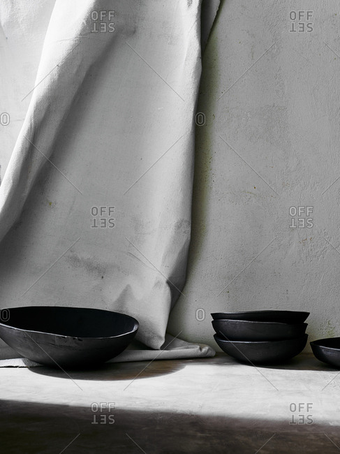 Handmade black ceramic dishes arranged against painted cloth backdrop
