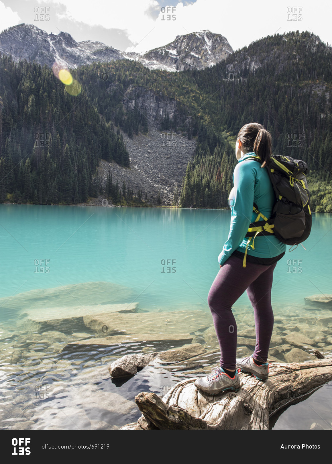 A women stands on a fallen tree next to Middle Joffre Lake and stares out at the surrounding peaks. The lake is a vibrant turquoise color due to glacier till. This hike is a popular one with in the Duffy Lake Provincial Park due to its stunning views and 