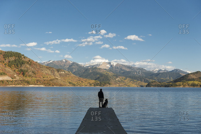Silhouette of man standing on lake jetty with German Shepherd and admiring beautiful landscape, Swan Valley, Idaho, USA