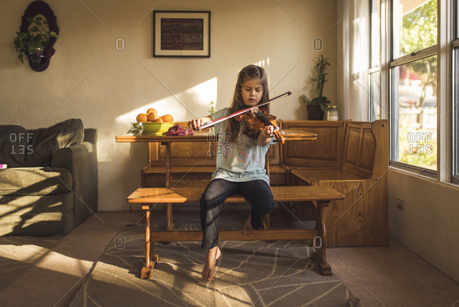 Girl playing violin while sitting on wooden seat at home