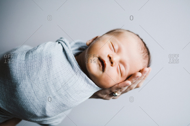 Newborn baby boy asleep swaddled in a light blue blanket against a light grey background