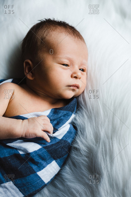 Top view of newborn baby boy awake swaddled in a blue checked blanket against a white fur background