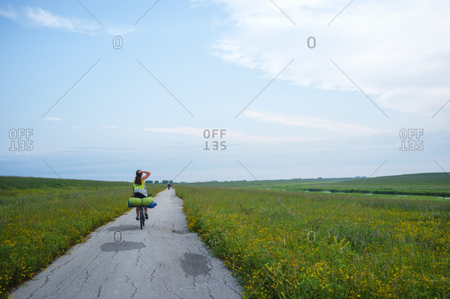 A female cyclist loaded with camping gear pedals through a vast grassy field