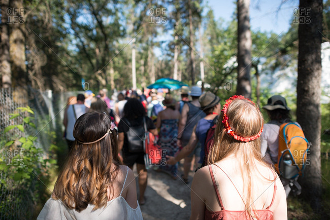 Festive concert goers walk through sunlight-dappled trees