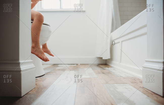 Bare feet and legs of toddler sitting on toilet stock 