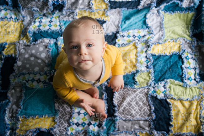 Baby boy sitting on quilt looking up