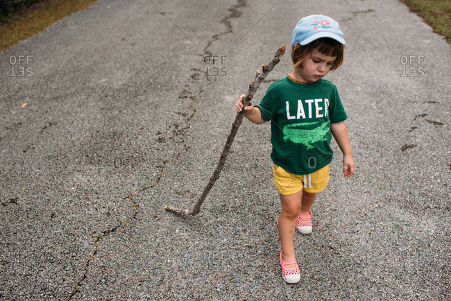 Little girl walking with a stick on a paved path
