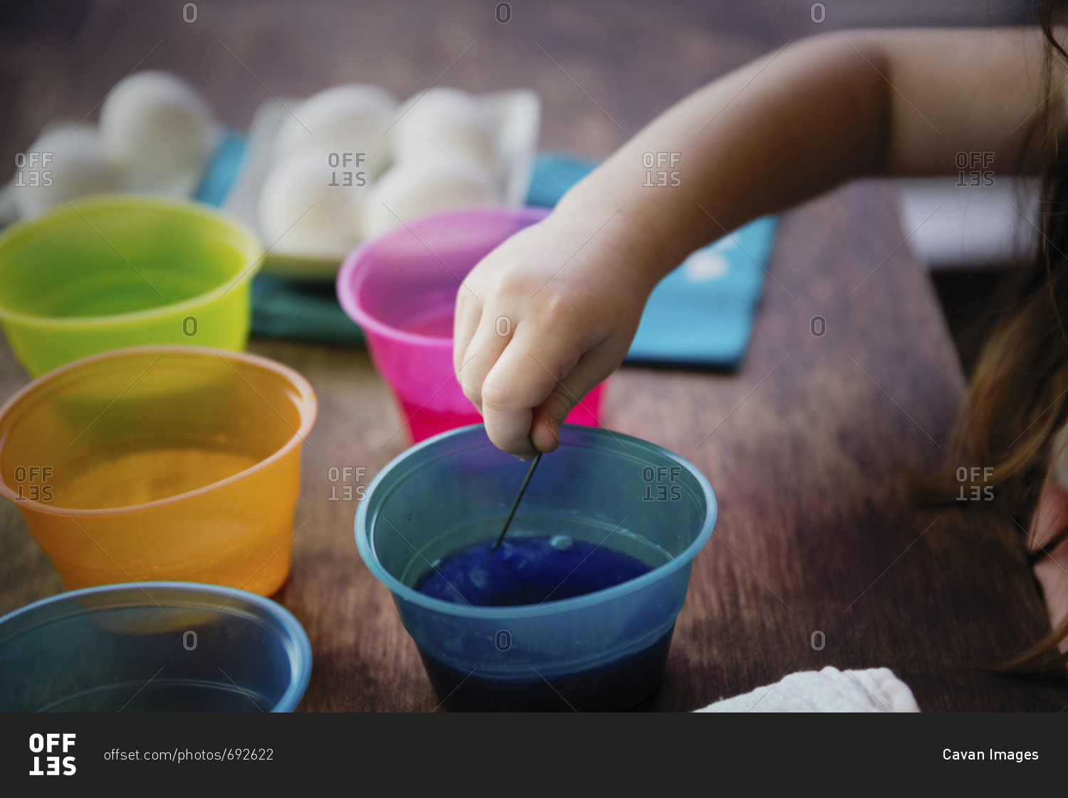 Cropped hand of girl using stirrer to mix dye in water for Easter Egg coloring on table