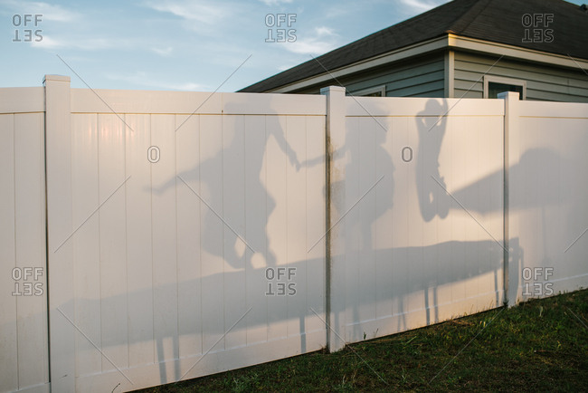 Kids jumping on trampoline casting shadow on backyard fence