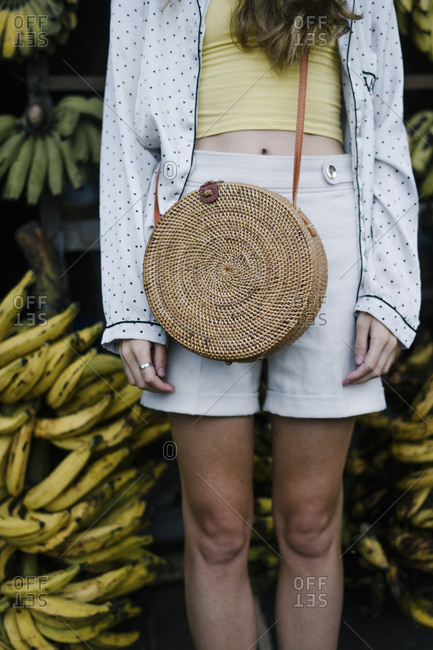 Bali visitor standing in front of bananas with wicker purse