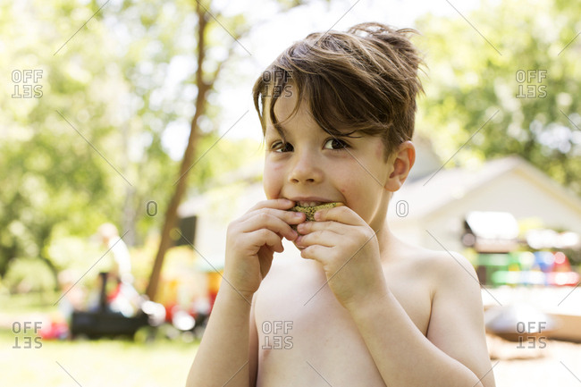 Young, shirtless boy chewing on a piece of melon outside