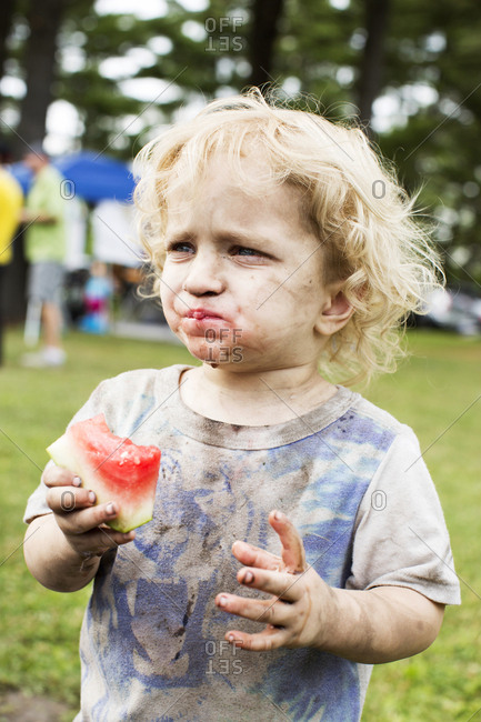 Dirty toddler eating watermelon outside