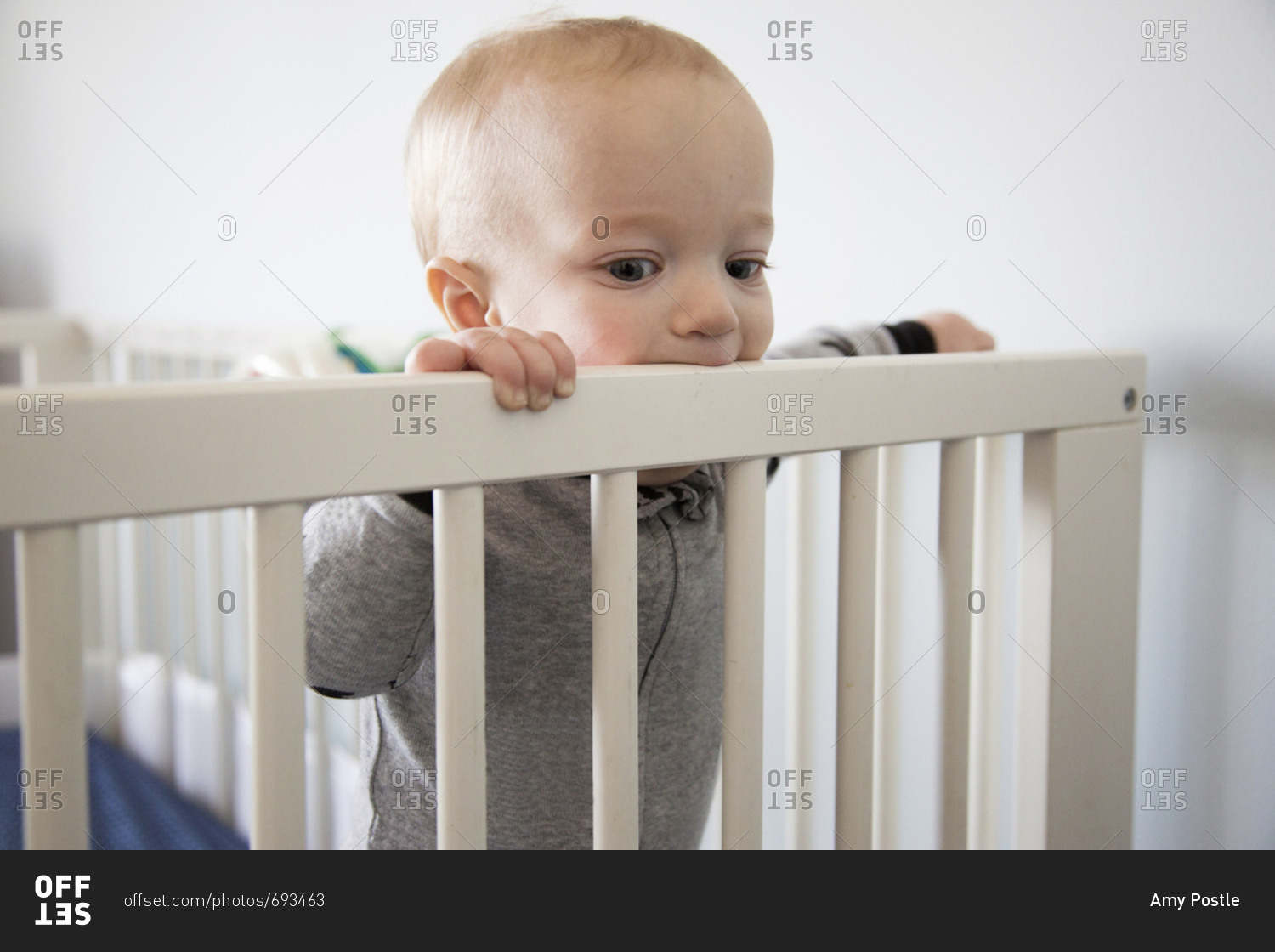 Baby standing up chewing on his crib rail stock photo OFFSET