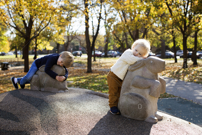 Two young brothers relaxing on animal sculptures in a park during fall