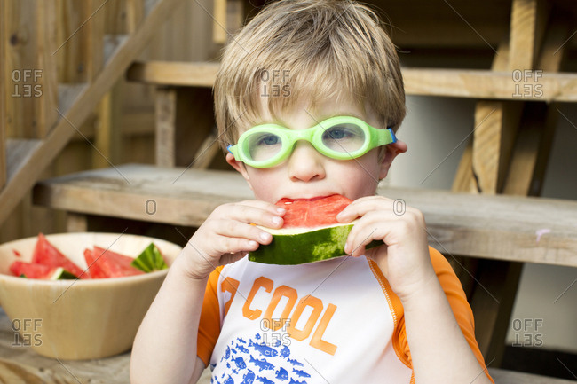 Little boy eating watermelon with goggles on outside