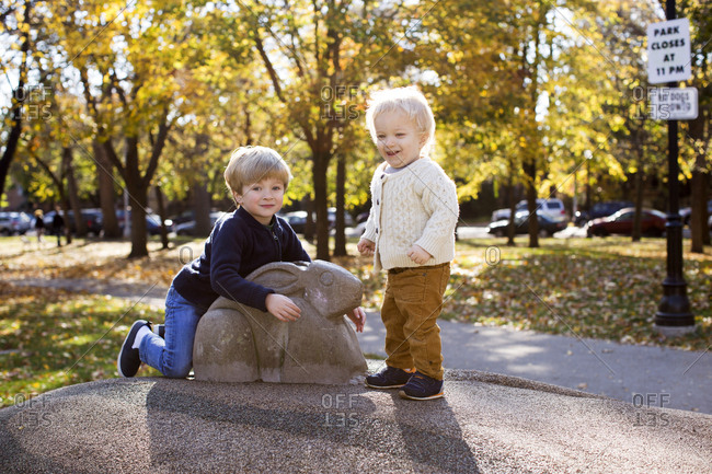 Portrait of two young brothers sitting on an animal sculpture in a park during fall