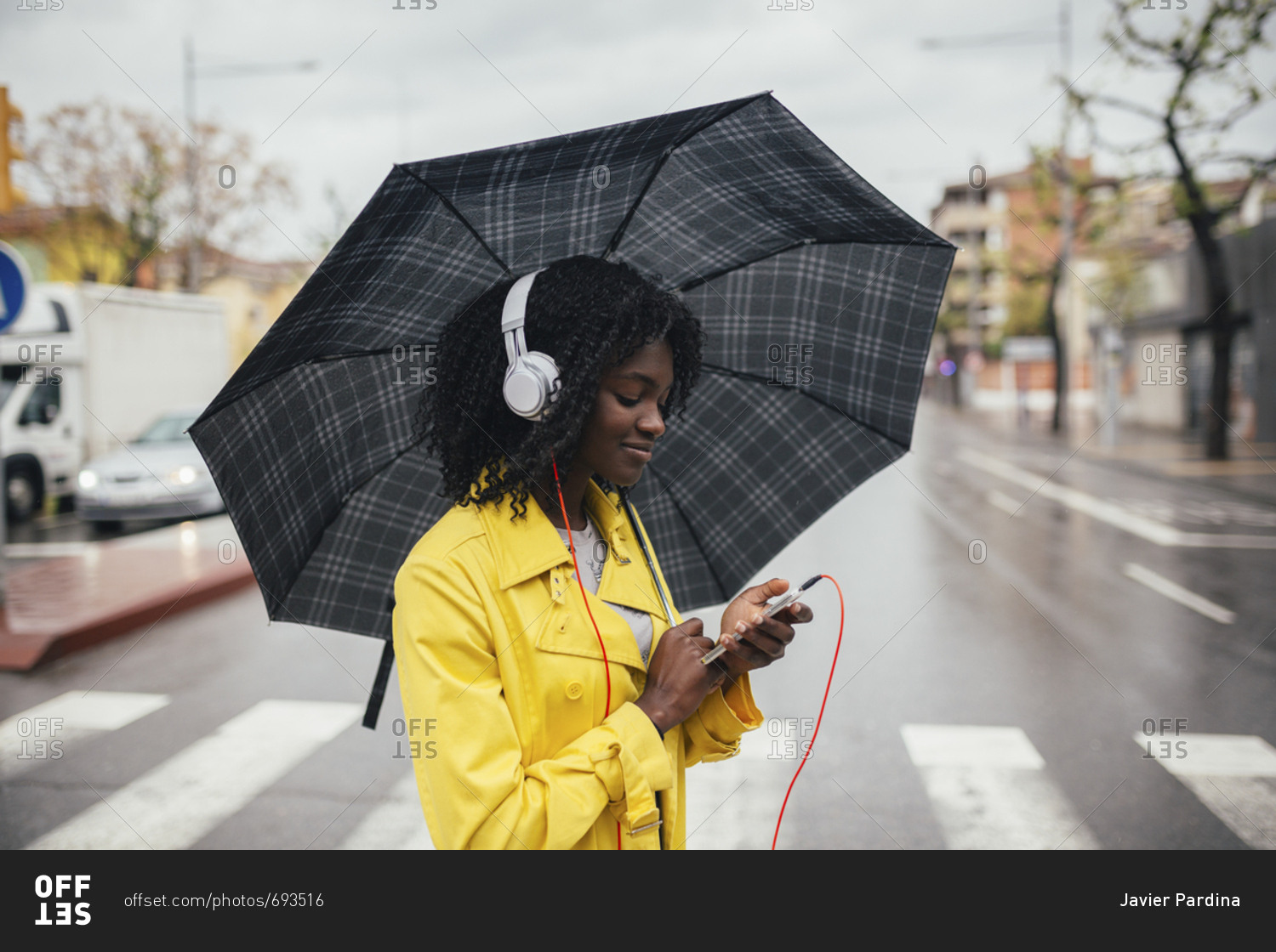 Young black woman looking down at phone while crossing the street in the rain