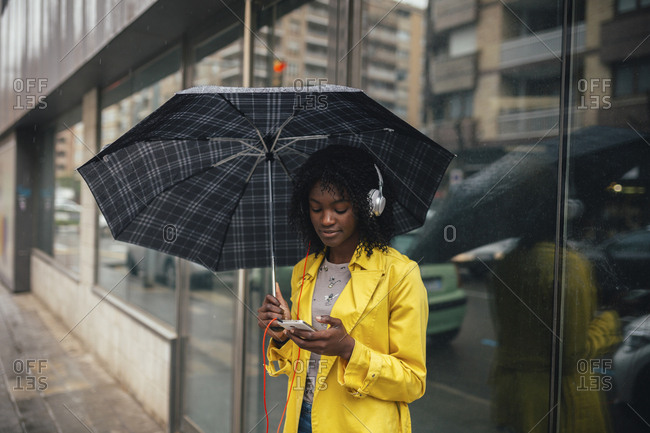 Young woman looking down at smartphone while waiting on the street in the rain