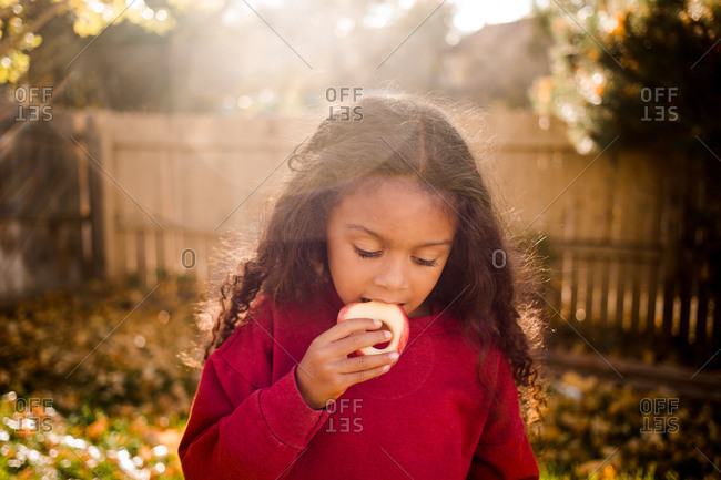 Little girl eating an apple outdoors in fall