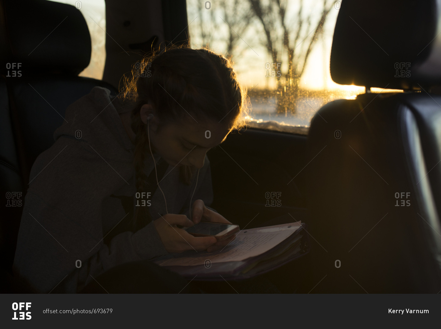 Teenage girl looking at smartphone in car over pile of homework