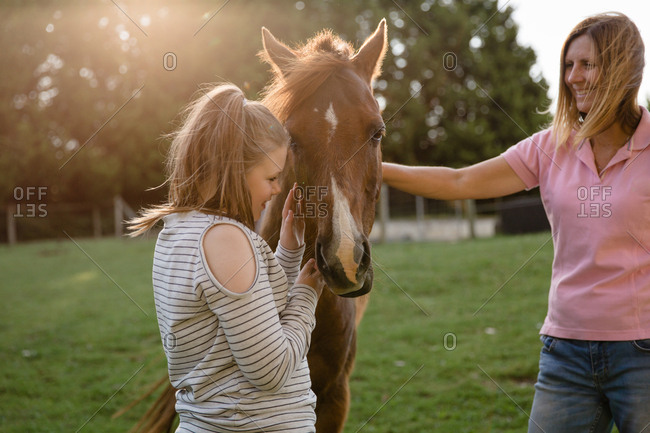 Girl petting horse under supervision of adult woman