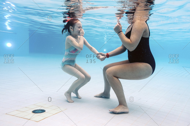 Low section of mother with daughter swimming underwater in pool