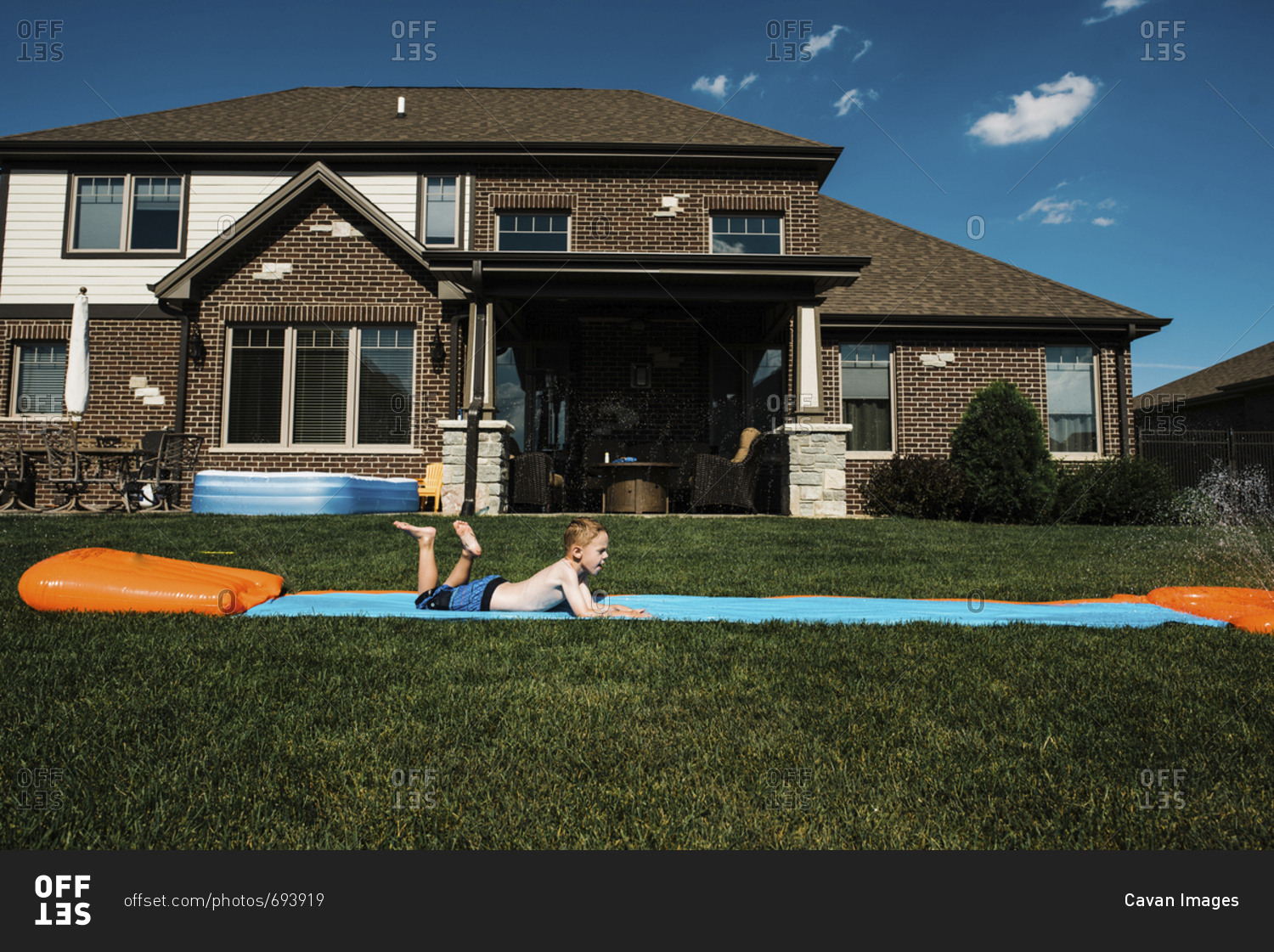 Side view of boy sliding on water slide mat in front yard