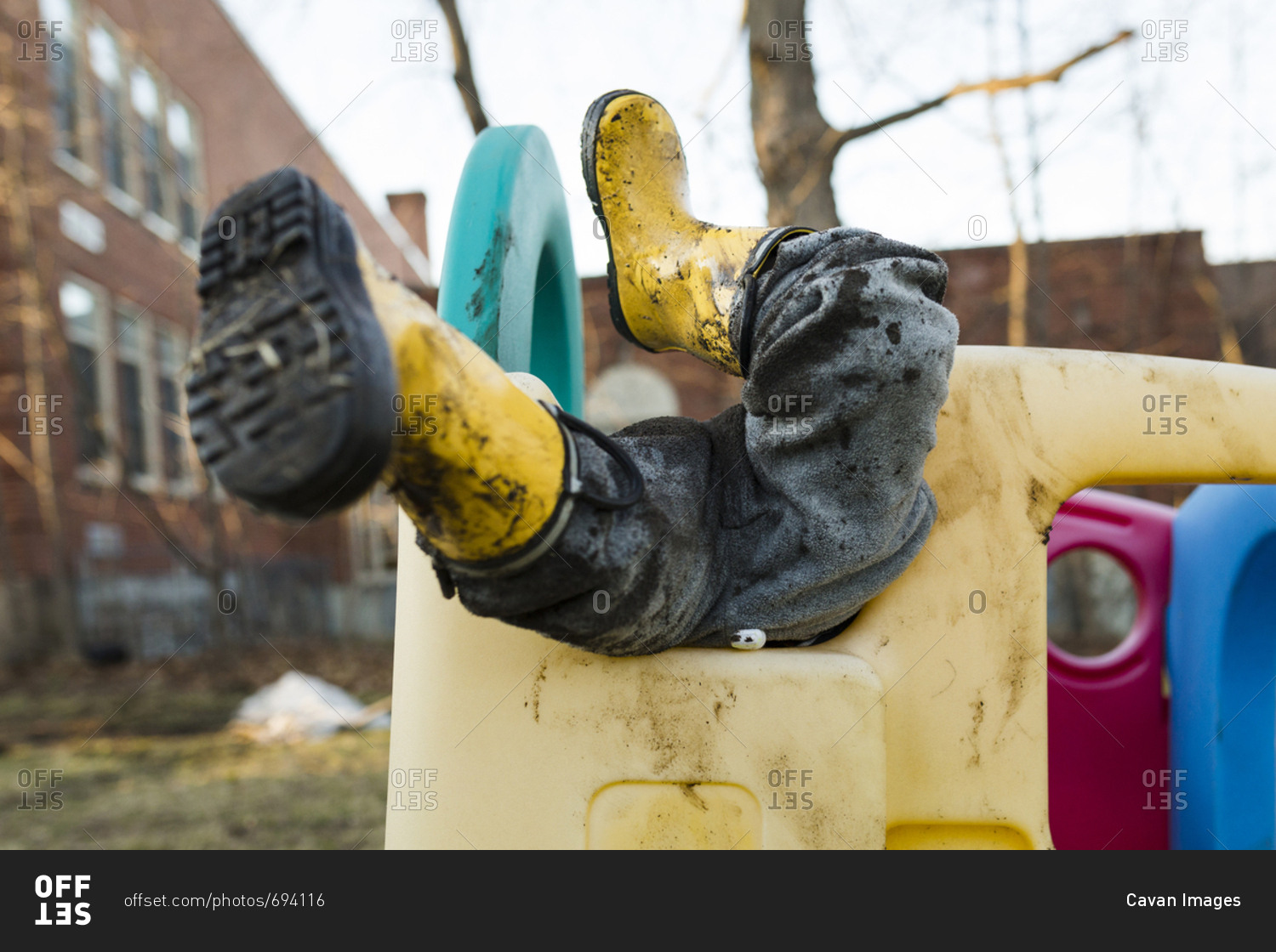 Low section of playful boy wearing muddy rubber boots while playing on outdoor play equipment at playground