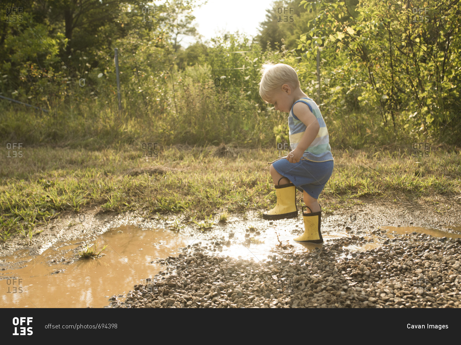 Side view of playful boy stamping foot in puddle at forest