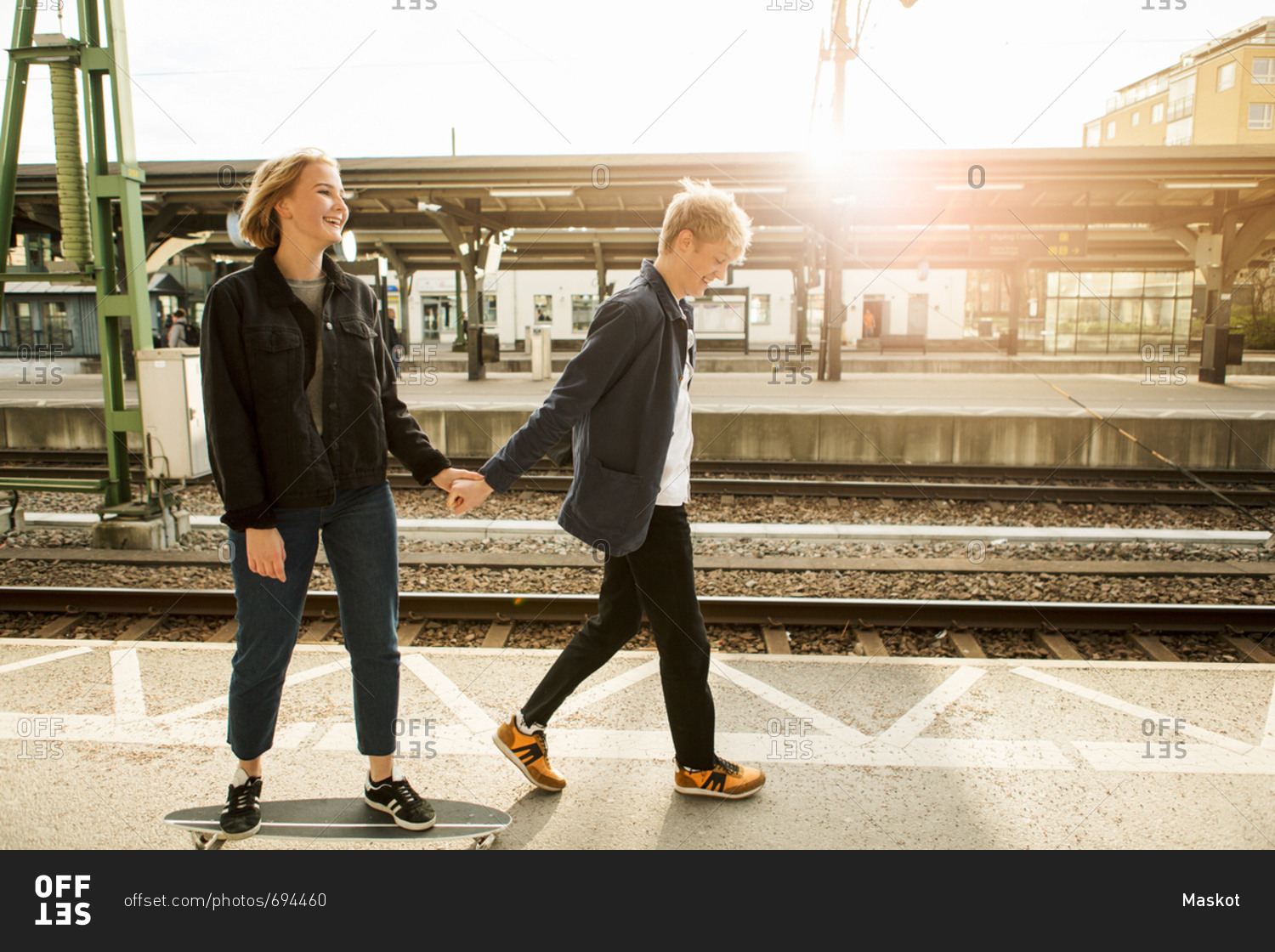 Full length of young man pulling teenage girl on skateboard at railroad station platform