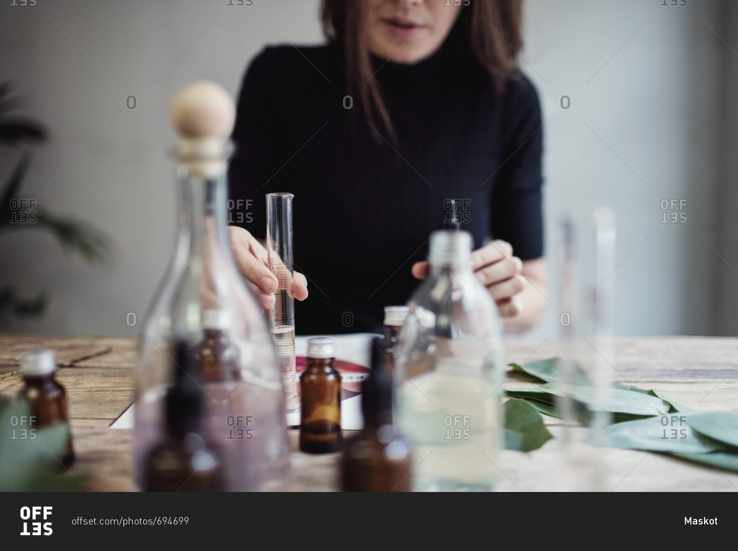 Midsection of female owner mixing liquid while sitting at table against wall in perfume workshop