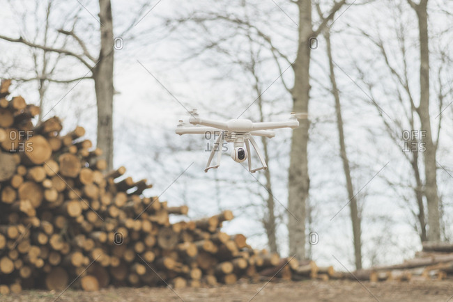 A quadcopter drone flies near a stack of logs