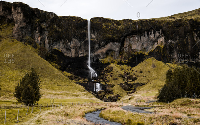Waterfall over steep cliff in grassy valley