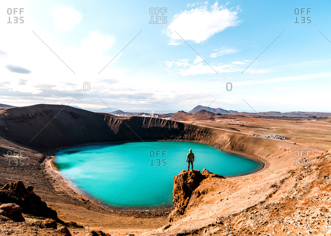 Person standing on rocky outcrop overlooking scenic lake in barren landscape