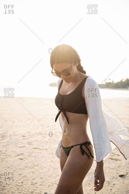 Young woman in swimsuit walking on the beach during sunset stock photo -  OFFSET