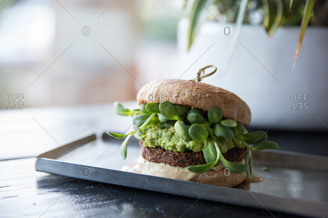 Veggie burger topped with guacamole and sunflower sprouts