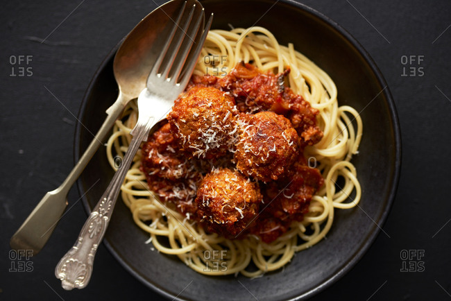 Top down view of homemade meatballs and spaghetti in dark bowl on dark background